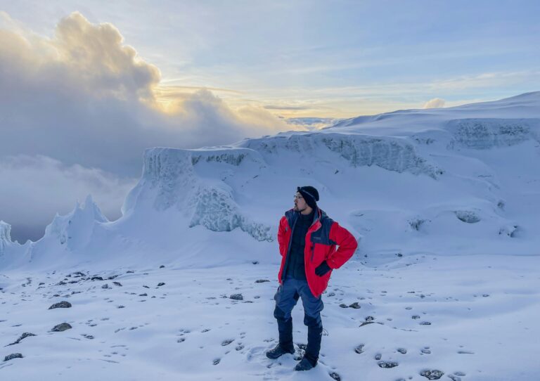Man in red jacket explores the snowy summit of Mt. Kilimanjaro, Tanzania at sunrise.
