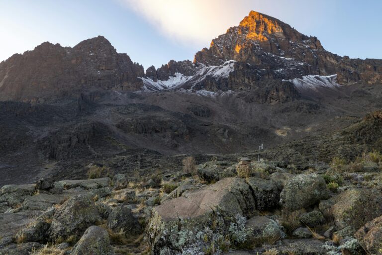 Stunning view of Mount Kilimanjaro's peak at sunrise, showcasing rocky terrain and snow patches.