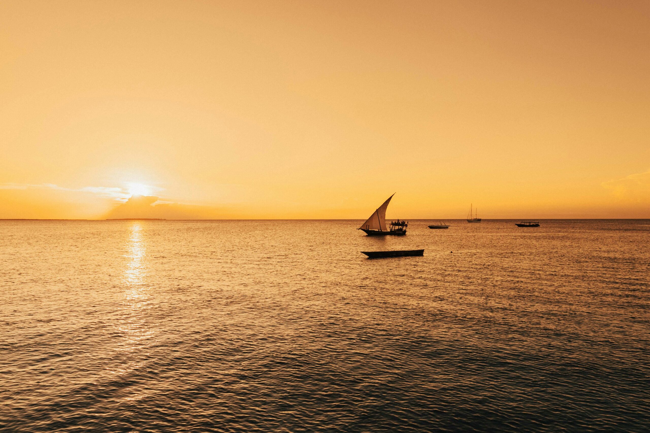 Serene sailboat scene with a golden sunset over the Indian Ocean in Zanzibar, Tanzania.