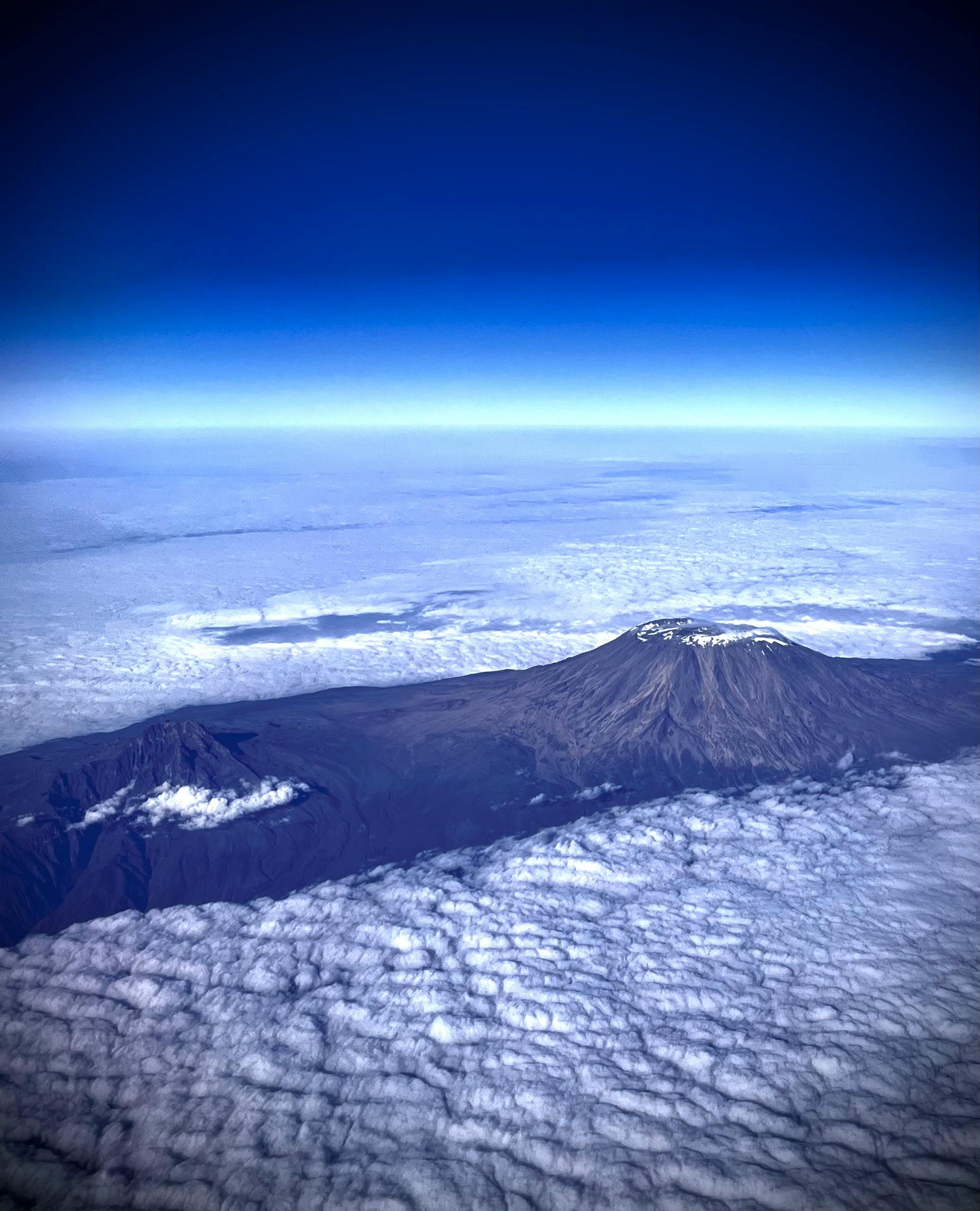 Stunning aerial view of Mount Kilimanjaro surrounded by clouds under a clear blue sky.